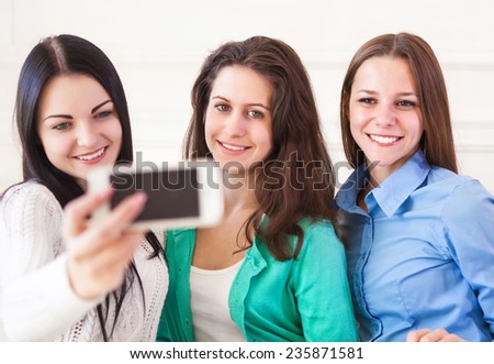 Three smiling teenage girls taking selfie with smartphone camera at home. Friendship, technology and internet concept