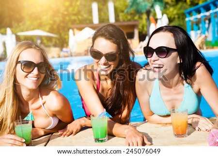 Happy girls with beverages on summer party near the pool