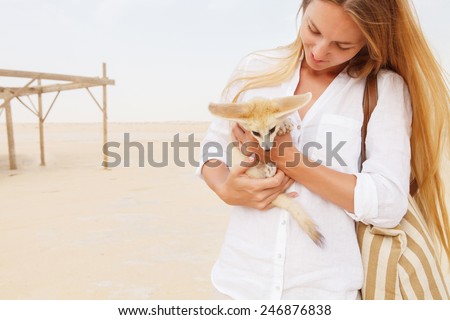 Young woman holding fennec fox in her hands during traveling in Sahara