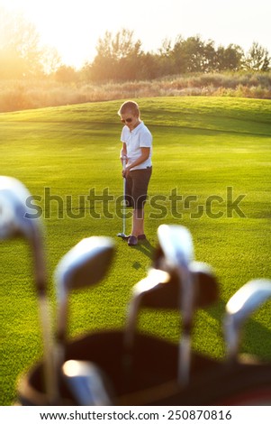 Casual kid at a golf field holding golf club. Sunset