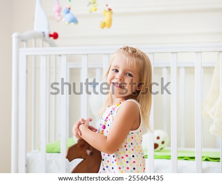 Little cute girl in nursery room with toys and wooden horse