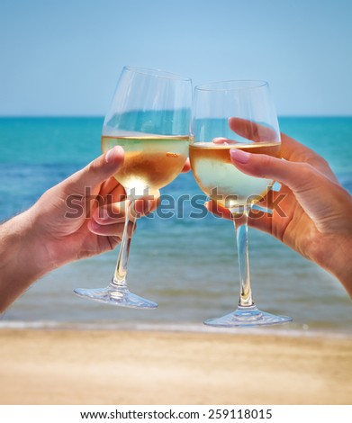 Man and woman clanging wine glasses with white wine at sky and sea background