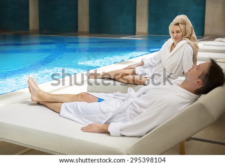 Young couple relaxing by the poolside wearing toweling robes