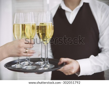 Professional male waiter in uniform serving champagne. Woman taking one glass of champagne. DOF. Natural light. Photo in motion