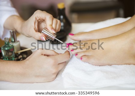 Woman in nail salon receiving pedicure by beautician. Close up of female feet resting on white towel