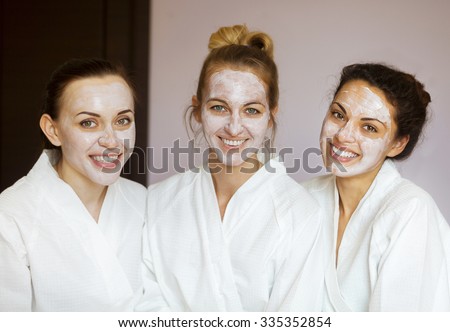 Three young happy women with face masks at spa resort. Frenship and wellbeing concept