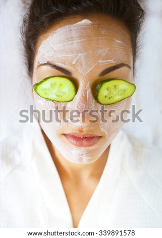 Young happy woman with a facial mask and cucumber on her face