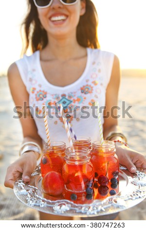 Happy young woman holding a dish with a drinks at summer beach party
