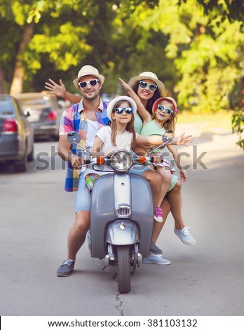 Happy young family riding a vintage scooter in the street wearing hats and sunglasses. Holiday and travel concept