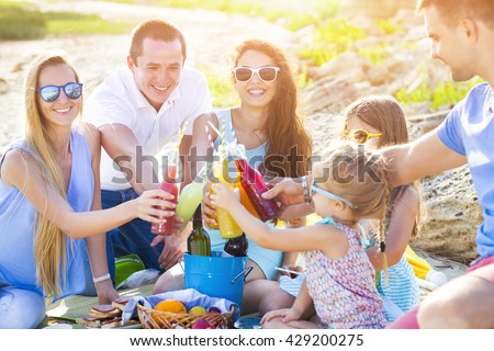 Friends sitting on the sand at the beach at the summer picnic with lemonade