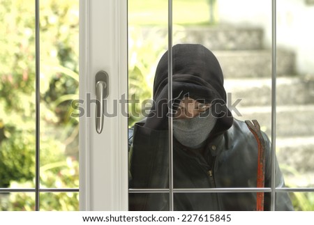 Burglar wearing black clothes and leather coat breaking in a house