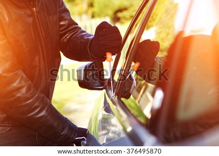 Thief wearing black clothes and leather coat stealing a car
