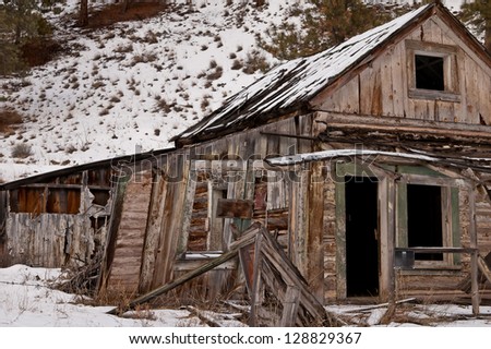 The front door of abandoned homestead is shown.  The scene is in the winter, a snow-covered mountain in Montana