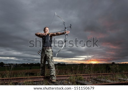Tough man with bow and arrows during dramatic cloudy sunset.