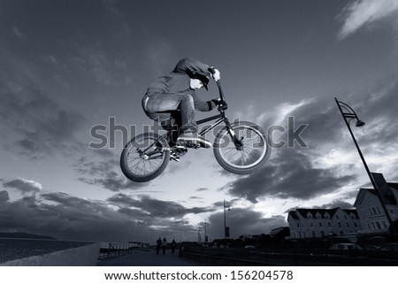 Young man performs BMX stunts during sunset at the street. Monochromatic