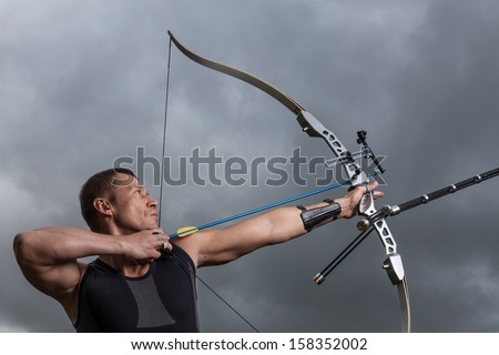 Tough man with bow and arrows, close up with cloudy sky at background.