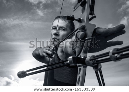 Tough man with bow and arrows, close up with cloudy sky at background. Monochromatic