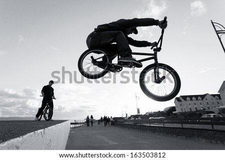 Two Young men performs BMX stunts during sunset at the street. Monochromatic