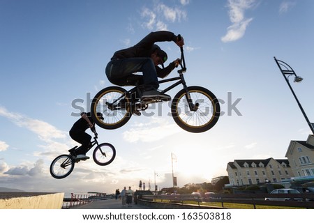 Two Young men performs BMX stunts during sunset at the street.