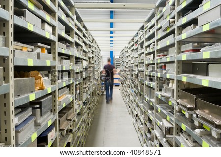 Metal Shelves With Spare Parts And Technician In Plant Interior