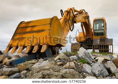 yellow excavator on top of big heap of stones, close up
