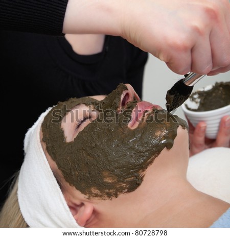 cosmetologist applying seaweed beauty mask at woman face