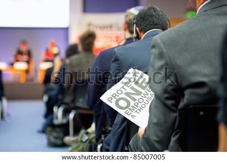 man  holding a poster with sign \'Protect One Empower a Thousands\' during presentation in busy  auditorium