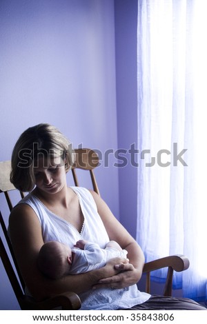 Mother rocking newborn baby in rocking chair next to window