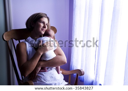 Mother holding newborn baby in rocking chair next to window