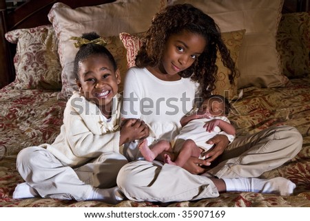 Happy little sisters with newborn baby sibling
