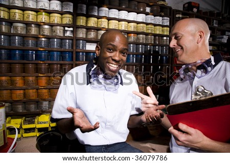 Male coworkers by shelves of colored inks in print shop