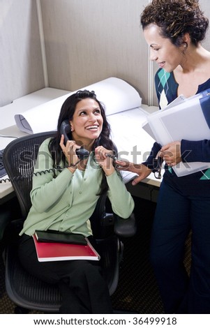 Two Hispanic female colleagues meeting in office cubicle