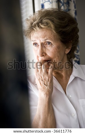 Sad elderly woman looking out window