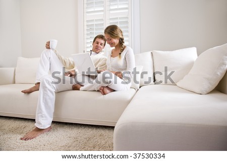 Father and teenage daughter on white living room sofa using laptop