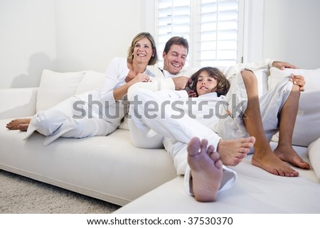Parents and son relaxing together on white living room sofa