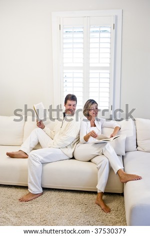 Mature couple relaxing and reading together on white living room sofa