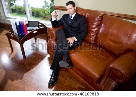 Serious confident businessman sitting on leather couch, staring at camera