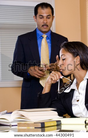 Young African-American female office worker reading papers in boardroom with middle-aged Hispanic businessman standing beside