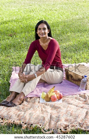 Mid-adult Indian woman sitting on picnic blanket on grass in park