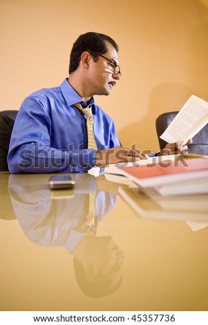 Middle-aged Hispanic businessman working in office reading reference book