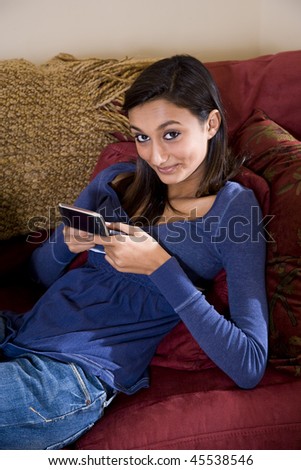 Pretty mixed-race Indian teenage girl relaxing at home on sofa texting on mobile phone