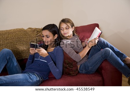 Teen girl texting on mobile phone while younger sister looks over her shoulder