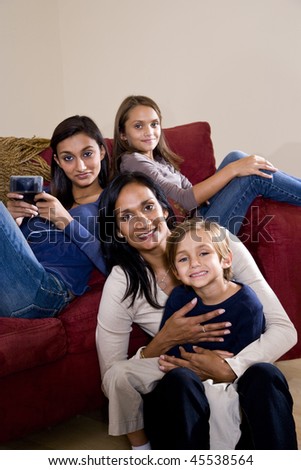 Family portrait of Indian mother with 3 mixed-race children sitting at home together on sofa