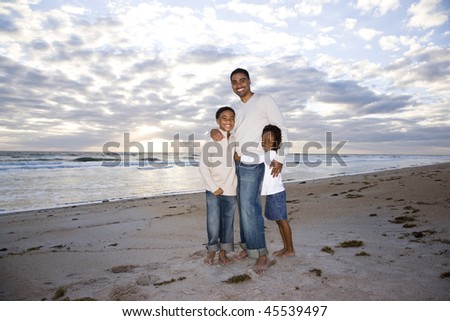 Happy African-American father,  ten year old son and six year old daughter standing on beach