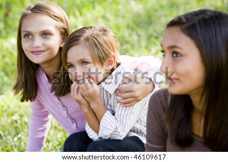 Cute 5 year old little boy with affectionate older sisters together on grass outdoors