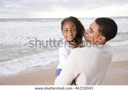 Happy African-American father holding six year old daughter at beach