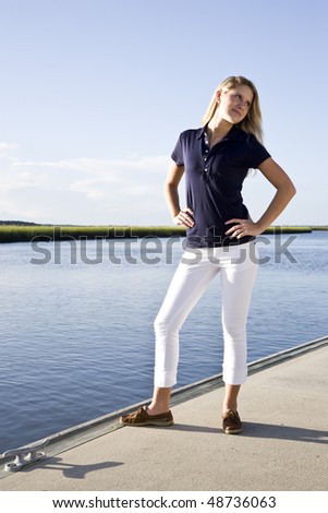 Teenage girl standing posed on dock by water on sunny day