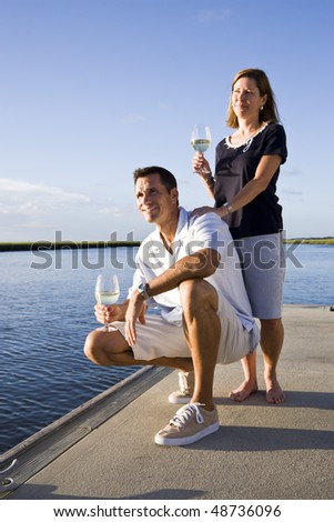 Mid-adult couple on dock by water enjoying drink on sunny day