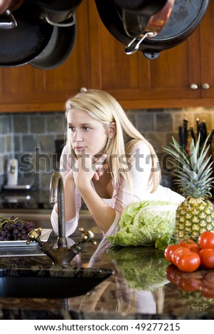 Pretty 17 year old teenage girl leaning on kitchen counter thinking