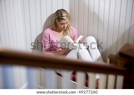 17 year old teenage girl reading alone in quiet corner by staircase